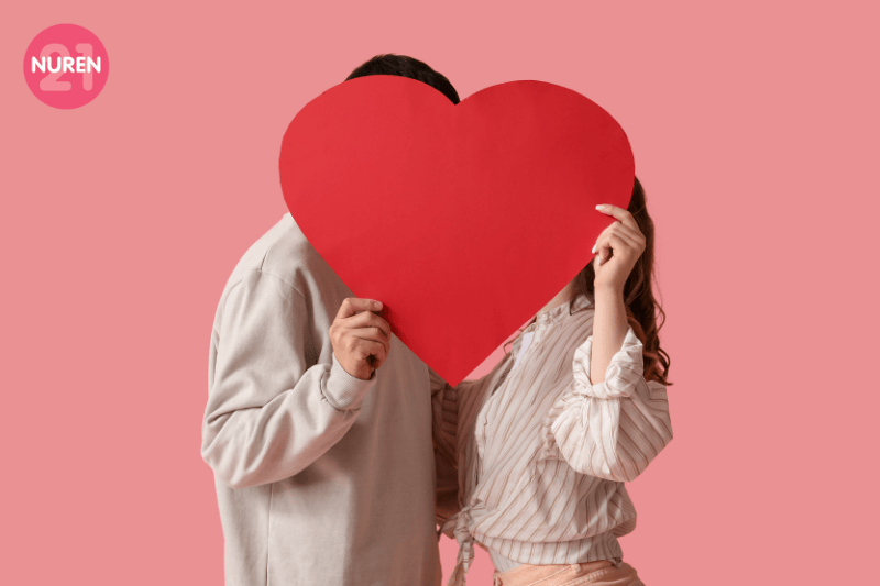 couple behind a big heart cutout in a pink isolated background